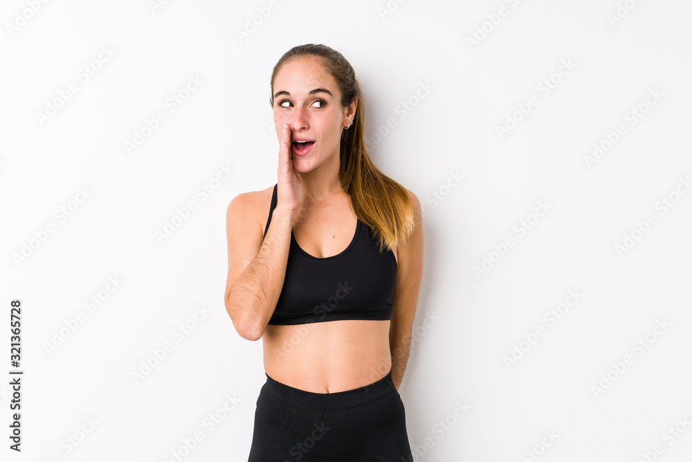 Young caucasian fitness woman posing in a white background is saying a secret hot braking news and looking aside Young caucasian fitness woman posing in a white background is saying a secret hot braking news and looking aside