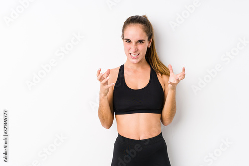 Young caucasian fitness woman posing in a white background upset screaming with tense hands.