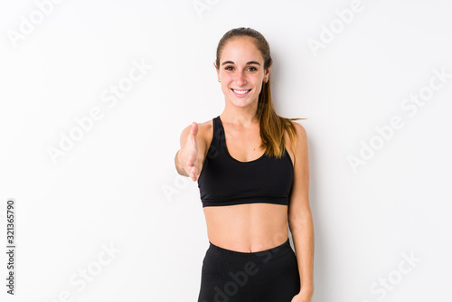 Young caucasian fitness woman posing in a white background stretching hand at camera in greeting gesture.