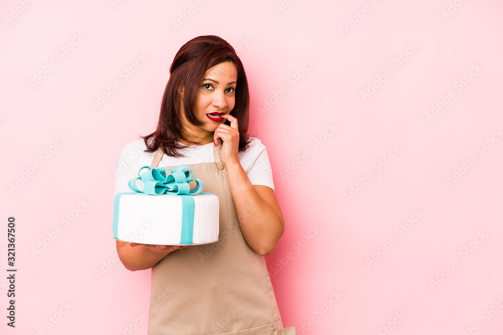 Middle age latin woman holding a cake isolated on a pink background relaxed thinking about something looking at a copy space. Middle age latin woman holding a cake isolated on a pink background relaxed thinking about something looking at a copy space.