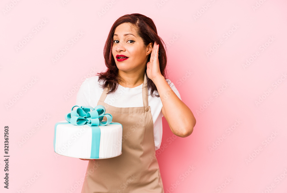Middle age latin woman holding a cake isolated on a pink background trying to listening a gossip. Middle age latin woman holding a cake isolated on a pink background trying to listening a gossip.