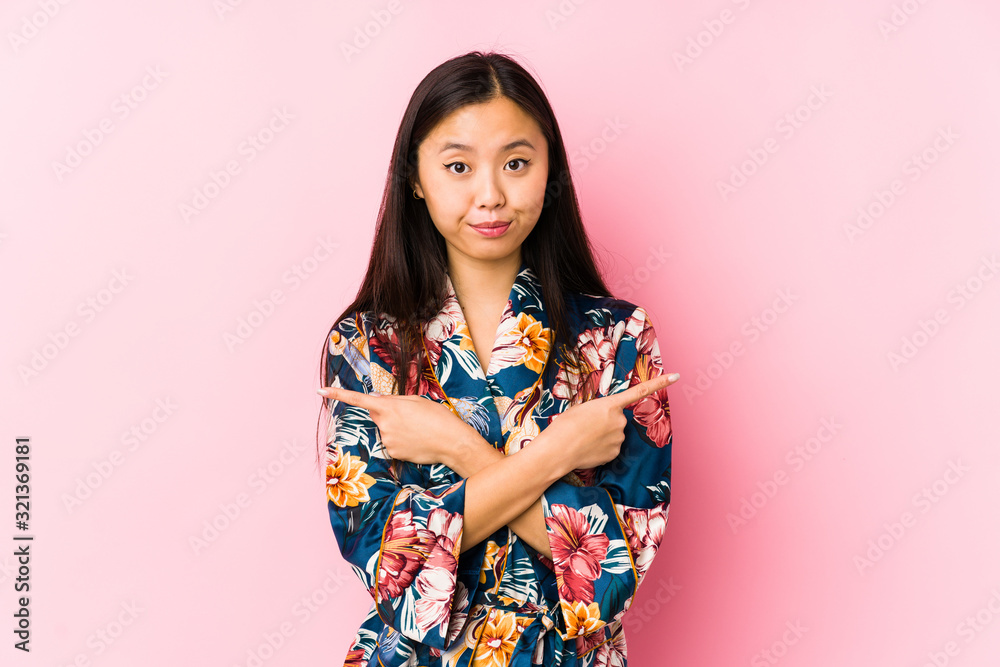 Young chinese woman wearing a kimono pajama isolated points sideways, is trying to choose between two options. Young chinese woman wearing a kimono pajama isolated points sideways, is trying to choose between two options.