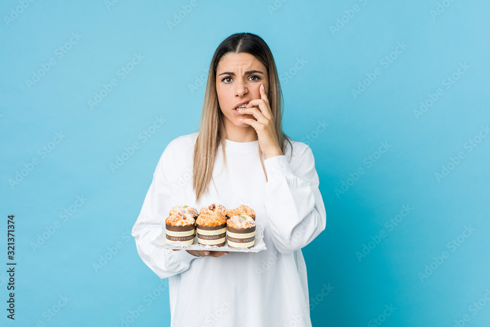 Young caucasian woman holding a sweets cake biting fingernails, nervous and very anxious. Young caucasian woman holding a sweets cake biting fingernails, nervous and very anxious.