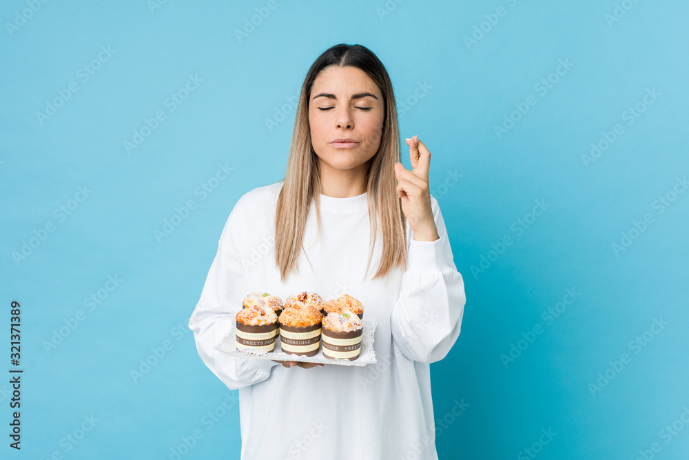 Young caucasian woman holding a sweets cake crossing fingers for having luck Young caucasian woman holding a sweets cake crossing fingers for having luck