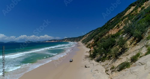 4k decending aerial view of the beach and 4x4 vehicles and coloured sand dunes near the township of Rainbow beach, the beach is accessible with a 4x4 vehicle dependent on tides,Queensland,Australia photo