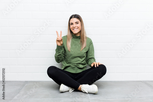 Young caucasian woman sitting on the floor showing number two with fingers.