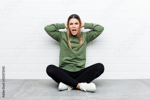 Young caucasian woman sitting on the floor covering ears with hands trying not to hear too loud sound.