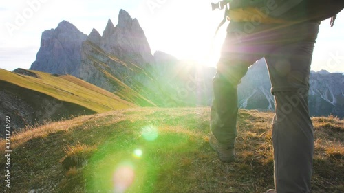 Young man hiking at Seceda mountain arriving to peak at sunrise. Backpack, yellow jacket, boots, beanie. Traveling to puez Odle, Dolomites, Trentino, Italy.