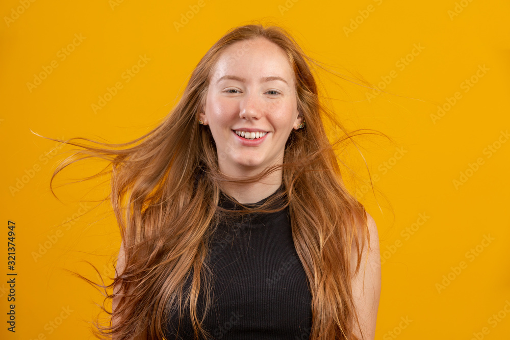 Fototapeta premium Portrait of beautiful cheerful redhead girl with flying hair smiling laughing looking at camera over yellow background.