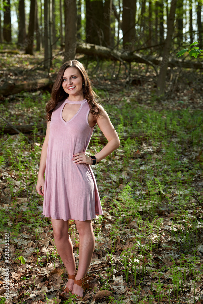 Gorgeous young Caucasian woman in pink cocktail dress stands in summer forest setting Gorgeous young Caucasian woman in pink cocktail dress stands in summer forest setting
