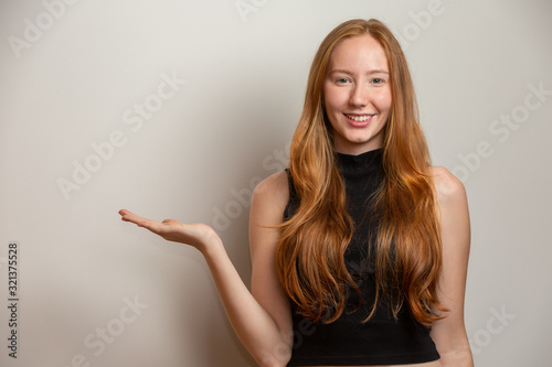 A redheaded girl on white studio background offers opportunities point finger side at copy free space for promotional content ad.