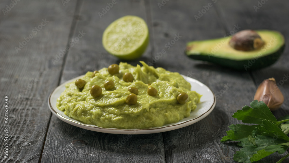 Guacamole with green peas in a white plate and herbs. Diet vegetarian Mexican food avocado. Guacamole with green peas in a white plate and herbs. Diet vegetarian Mexican food avocado.