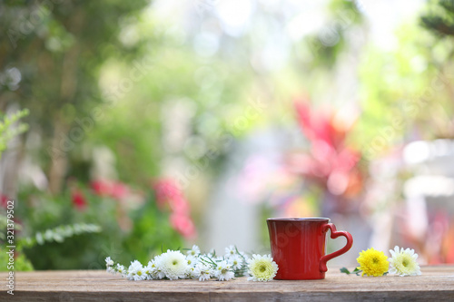 Red coffee mug with daisy and Chrysanthemum flower on wooden table front view at out door