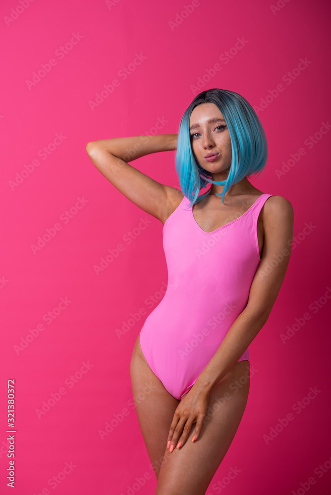 Pretty woman in a pink monokini and blue wig in the studio. Girl with artificial short hair posing in a colored swimsuit. Pretty woman in a pink monokini and blue wig in the studio. Girl with artificial short hair posing in a colored swimsuit.