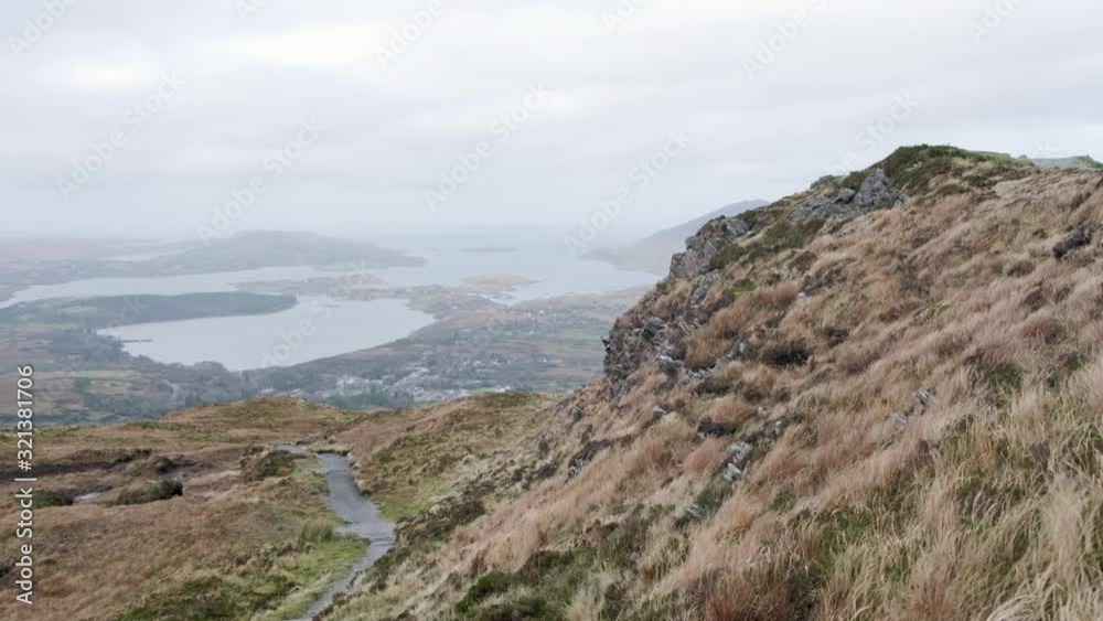 Super wide shot of Connemara National Park. Hill with moving grass in the foreground. Lake and ocean in the background. A path leads to the bottom of the valley. View from diamond hill. Super wide shot of Connemara National Park. Hill with moving grass in the foreground. Lake and ocean in the background. A path leads to the bottom of the valley. View from diamond hill.