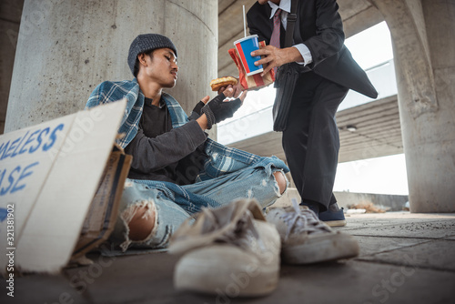 Businessman came up and help homeless man sitting on the floor. Help, money,food donation to vagrant male in the street
