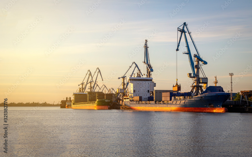 Cargo ship being loaded up by a crane with containers at port of Riga, Europe, sunset, evening view, industrial port