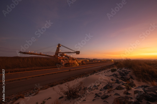 Wide angle picture mining industry equipment reclaimer machine, conveyor belts moving raw copper, silver, gold, from train load out stockyard export to ship load out areas with sunset the background 