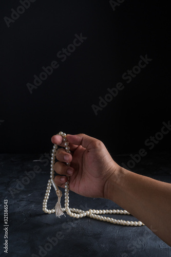 Faith in Islam,hand holding rosary beads on dark background. Islamic holiday celebration Eid Mubarak or Ramadan Kareem concept. Copy space. photo