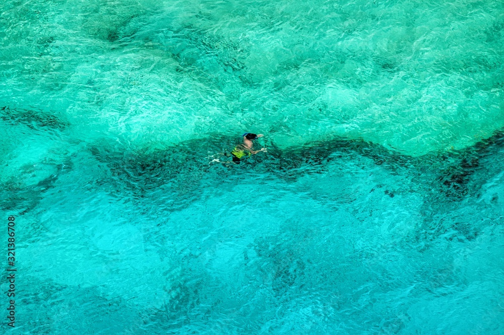 A single solo swimmer swims along a water shelf in clear blue tropical water as seen from above. 