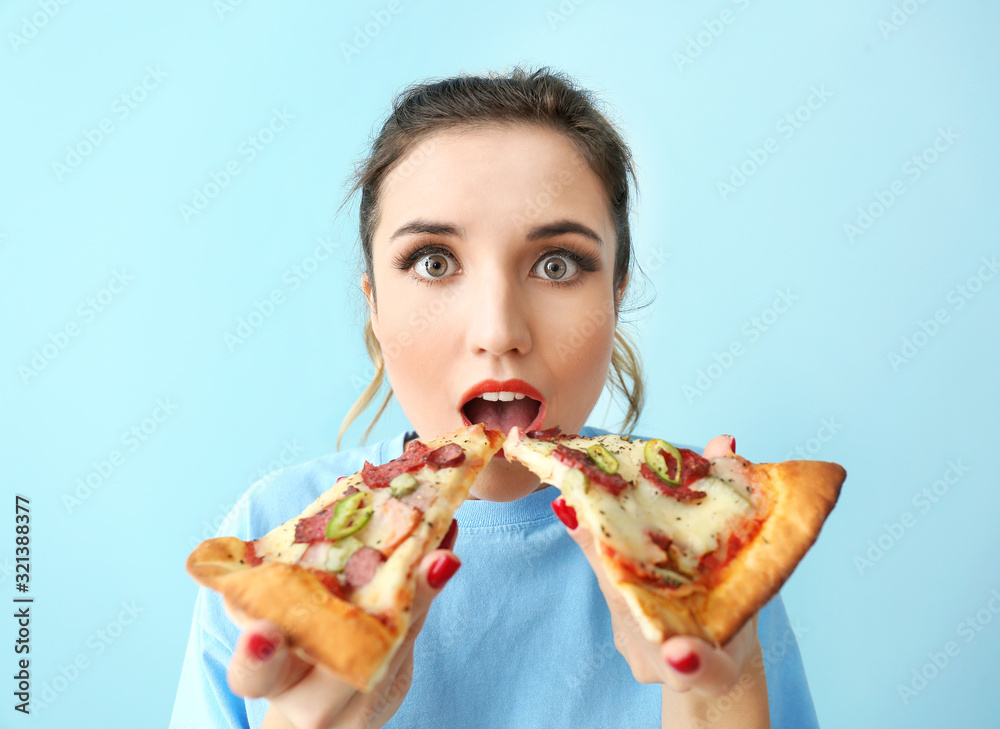 Portrait of beautiful young woman eating tasty pizza on color background