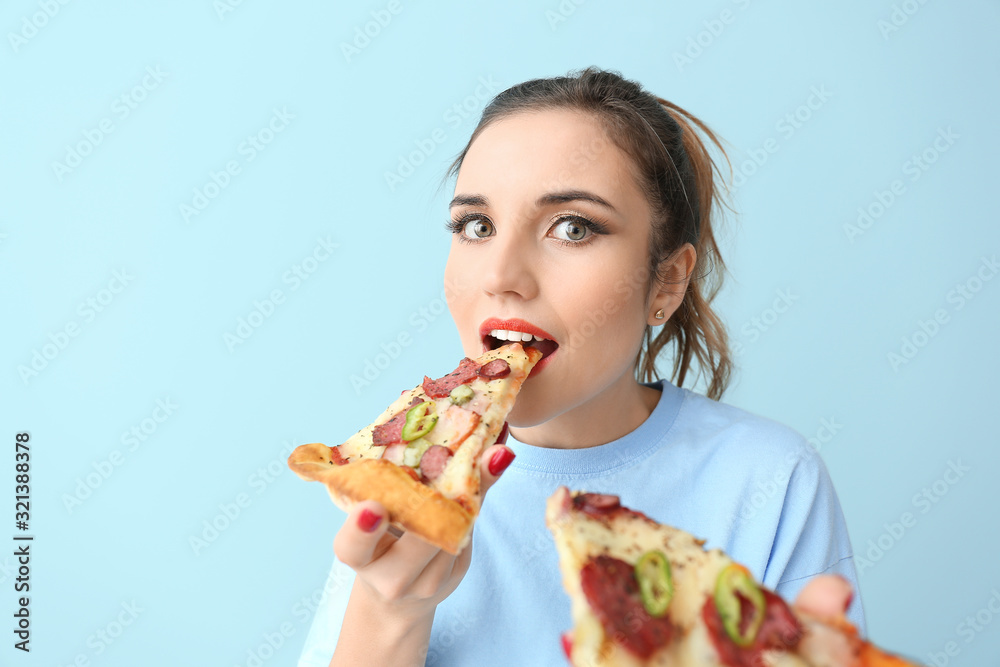Portrait of beautiful young woman eating tasty pizza on color background