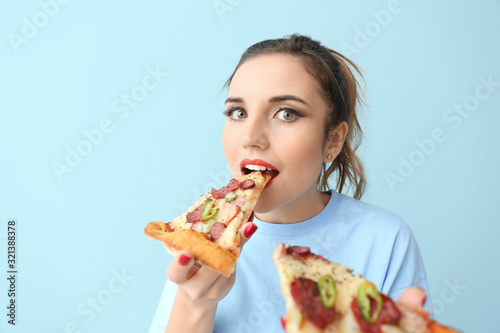 Portrait of beautiful young woman eating tasty pizza on color background