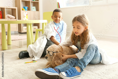 Cute little children dressed as doctors playing with dog at home