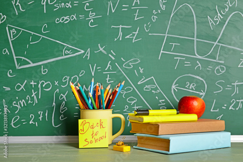 Set of school supplies and apple on table near blackboard