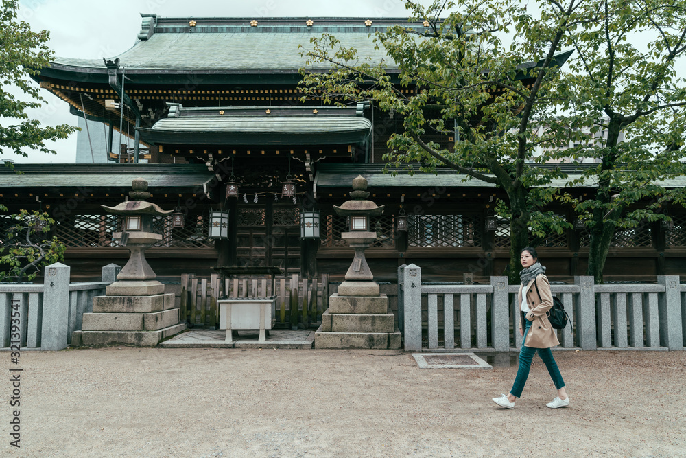 full length side view of elegant young girl traveler with backpack walking by Osaka Tenmangu Shrine in japan. traditional religion japanese shinto with trees and garden surround by two stone lantern