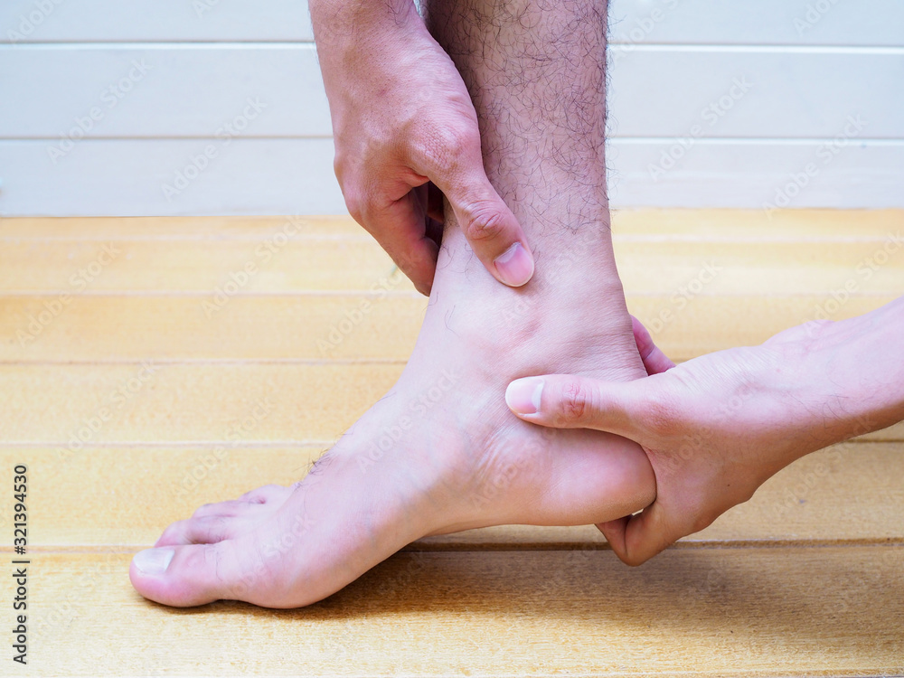 Young Asian man suffering from foot, leg and ankle pain, isolated on gray background. Young Asian man suffering from foot, leg and ankle pain, isolated on gray background.