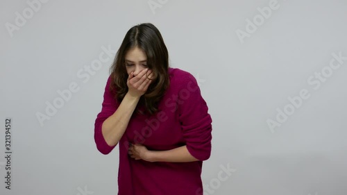 Sick brunette woman clutching belly suffering abdominal cramps and nausea, vomiting, symptoms of stomach flu or poisoning, gastrointestinal disorder . indoor studio shot isolated on gray background photo