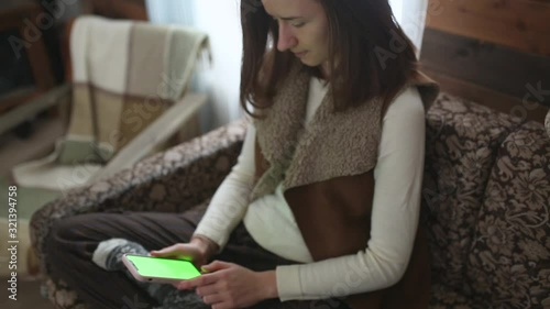 A lady scrolls a phone sitting on a sofa in a wooden house. Chromakey.