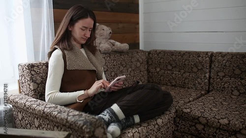 A lady scrolls a phone sitting on a sofa in a wooden house.