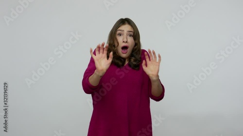 Phobia. Frightened brunette woman in pullover shaking and screaming from fear, freaked out gesturing to defend herself, looking terrified and scared. indoor studio shot isolated on gray background photo