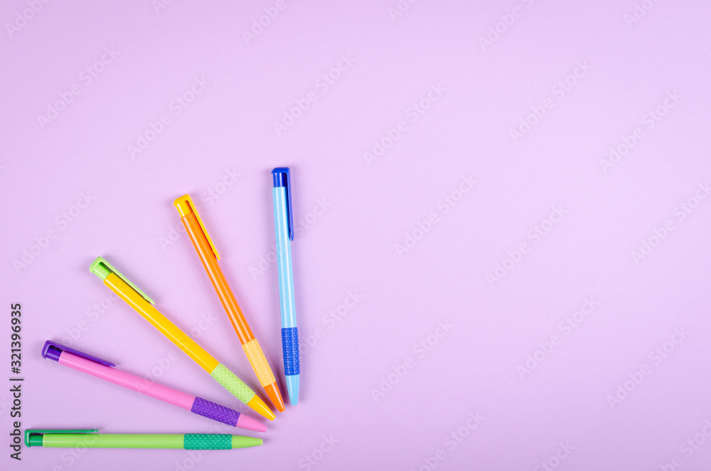 Different colored pens, school ballpoint on purple background composition.
