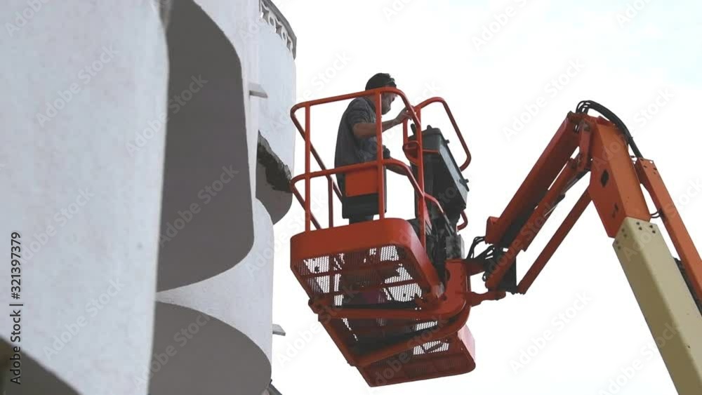 Mature man on a telescopic boom lift platform approaches a wall in to make repairs, in slow motion. Work concept.