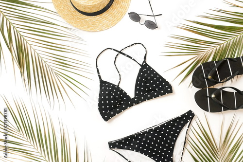 Woman's swimwear and beach accessories flat lay top view on white background. black and white polka dot bikini swimsuit, straw hat, shoes, sunglasses, palm leaf, sheels. Copy space photo