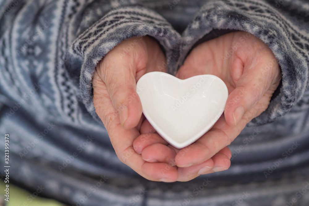 Close-up shot of a heart shaped white ceramic in the hands of an elderly woman. Heart and Health care concept Close-up shot of a heart shaped white ceramic in the hands of an elderly woman. Heart and Health care concept