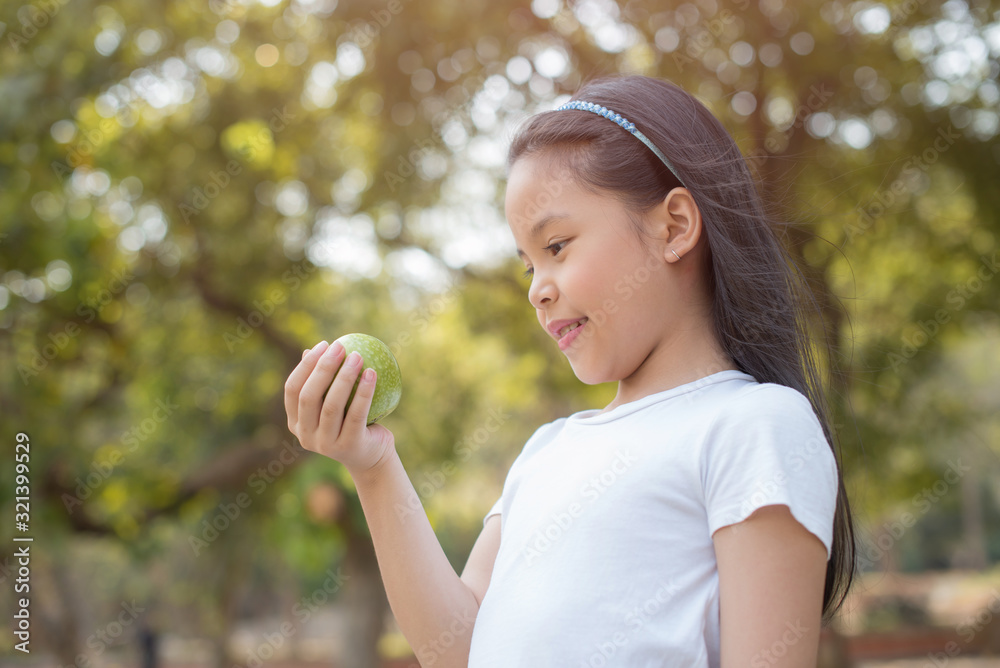 photo happy Little asian girl child standing with big smile. holding green apple in your hand.fresh healthy green bio background with abstract blurred foliage and bright summer sunlight photo happy Little asian girl child standing with big smile. holding green apple in your hand.fresh healthy green bio background with abstract blurred foliage and bright summer sunlight