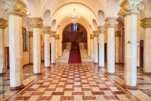 Large hall with white columns and a square checkered red tile pattern on the floor