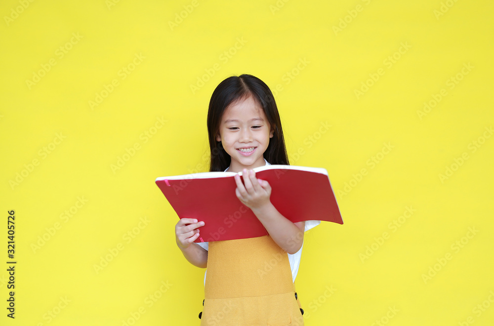 Asian little child girl reading book isolated on yellow background. Portrait of schoolgirl smiling while study. Back to School and education concept Asian little child girl reading book isolated on yellow background. Portrait of schoolgirl smiling while study. Back to School and education concept