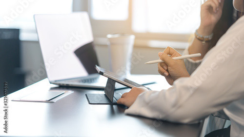 Two young business women sitting at table. First woman holding stylus pen with digital tablet screen. close up side view.