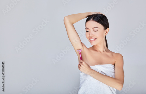Cute young Asian woman shaves her armpit on a gray background.