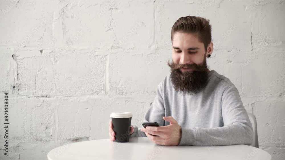 Happy bearded man sits at a Desk with a telephone at table and drinking coffee Happy bearded man sits at a Desk with a telephone at table and drinking coffee