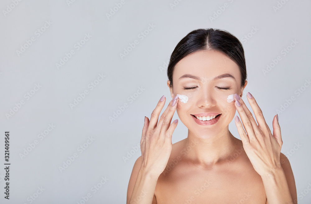 A cute Asian woman closing her eyes apply cream for her face.