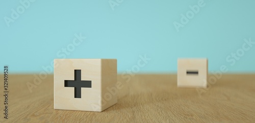 wooden cubes or dice with black plus  foreground and minus sign in the background on wooden table