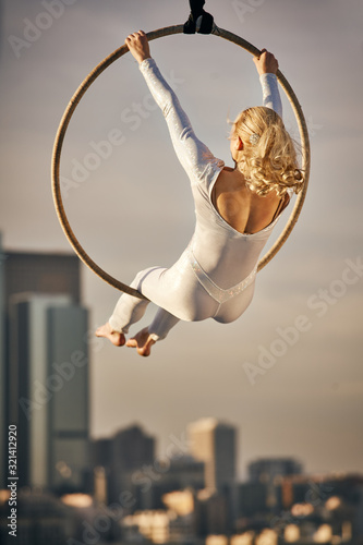 Young Woman Sitting in a Large Hoop Suspended in Air with Dramatic Cityscape in the Background in Golden Hour Sunset photo