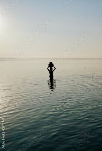 silhouette of a boy holding a bamboo jar above the head, standing in the water at sunrise