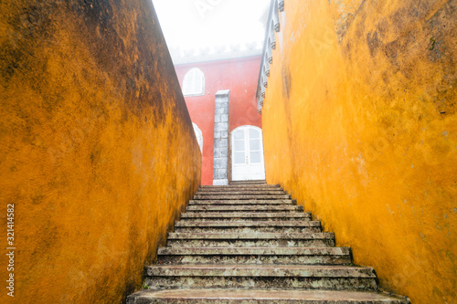 Fototapeta Naklejka Na Ścianę i Meble -  Extremely heavy, thick fog at the colorful Pena Palace in the winter. View of the steep steps with red and yellow walls